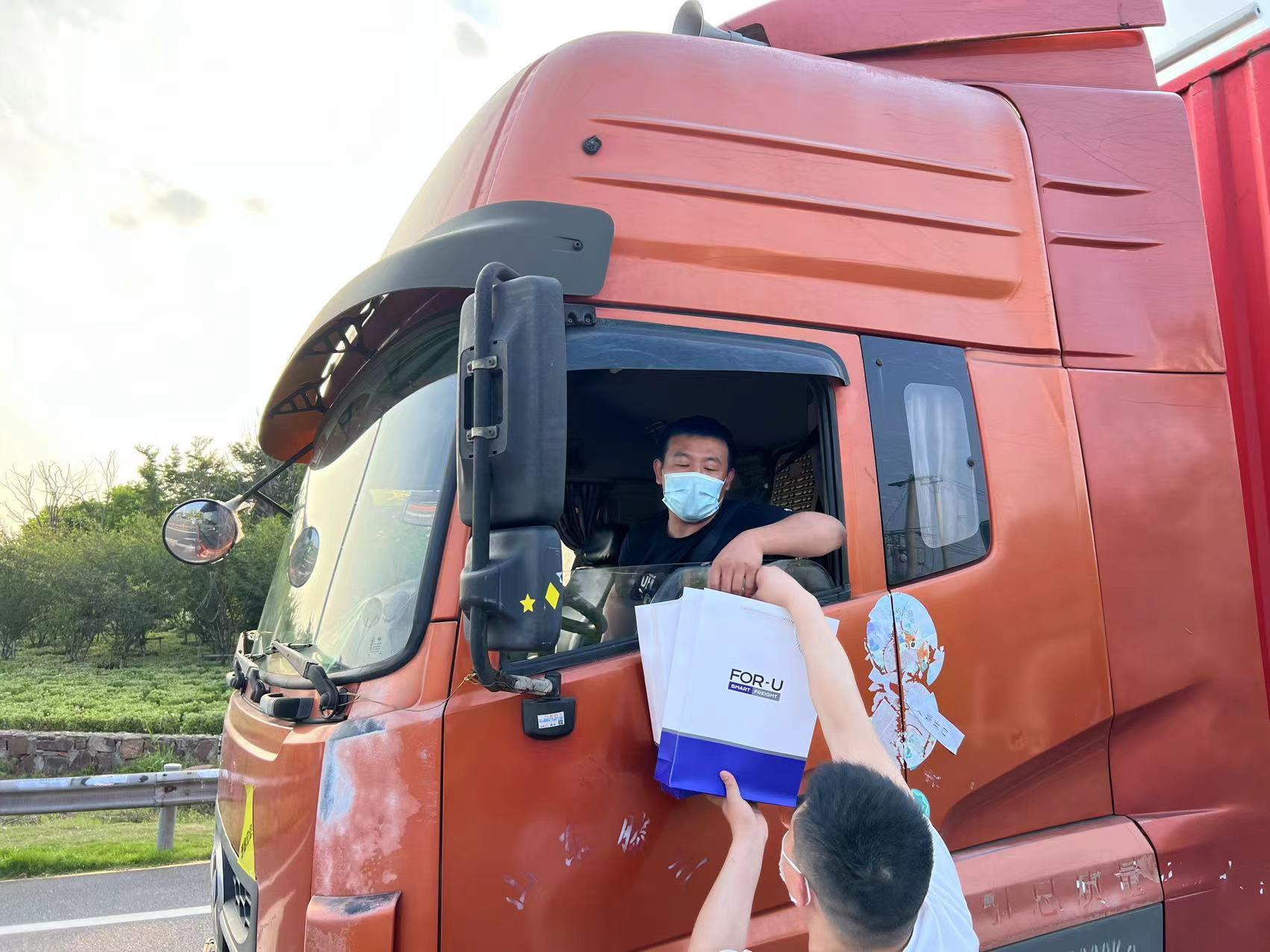 来自山东的卡车司机陶师傅在驾驶室接住福佑卡车工作人员递上的物资